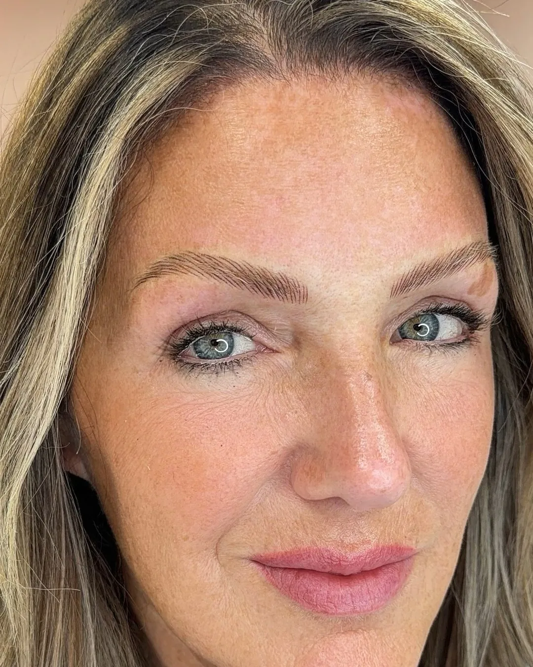 Healed nano brows on a client facing the camera, fine machine-made strokes with a soft arch